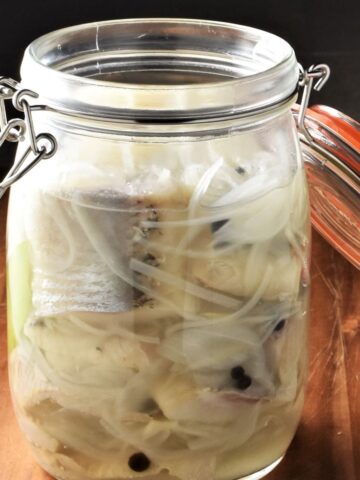 Close-up view of pickled herring with onion and spices in open jar.
