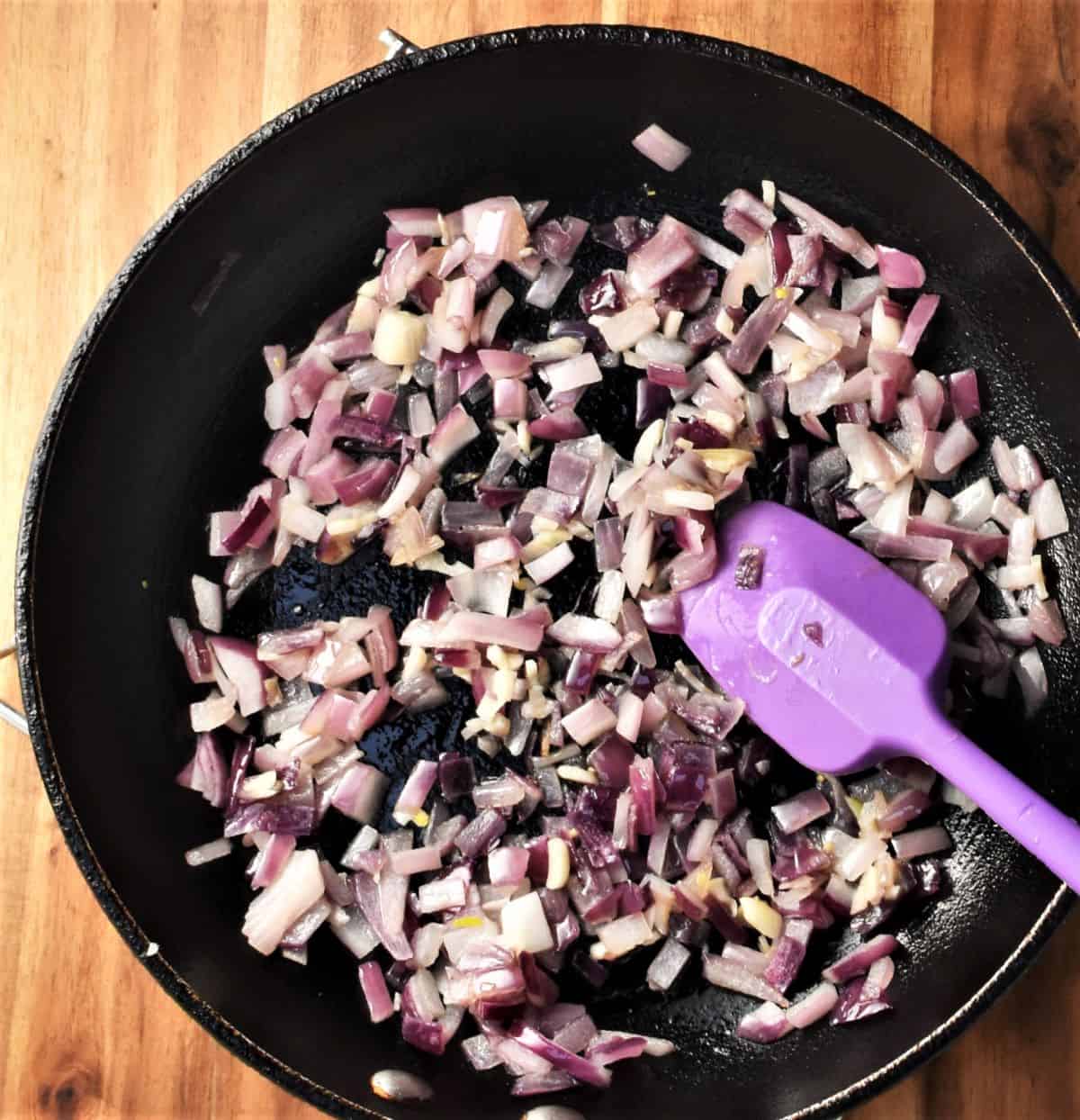 Frying red onion in pan with purple spatula.