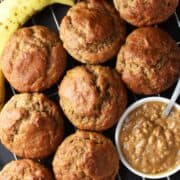Top down view of cluster of banana peanut butter muffins with ripe banana and crunchy peanut butter in white dish in background.