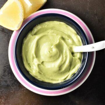 Top down view of creamy avocado mayo with spoon in black dish.
