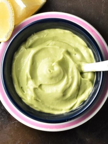 Top down view of creamy avocado mayo with spoon in black dish.