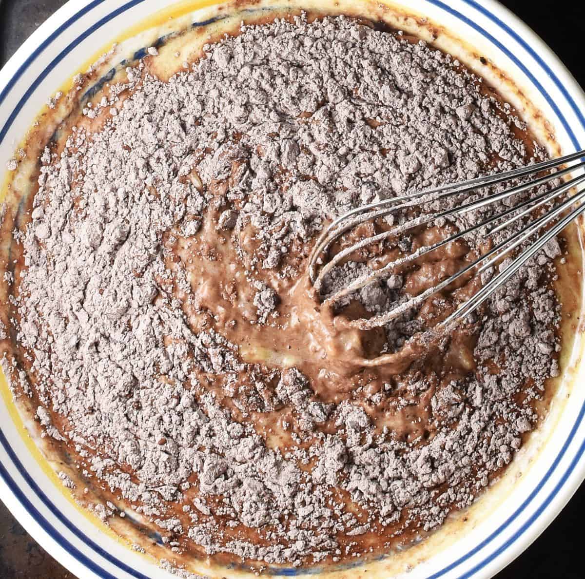 Chocolate banana pancake mixture with dry ingredients in shallow bowl with whisk.