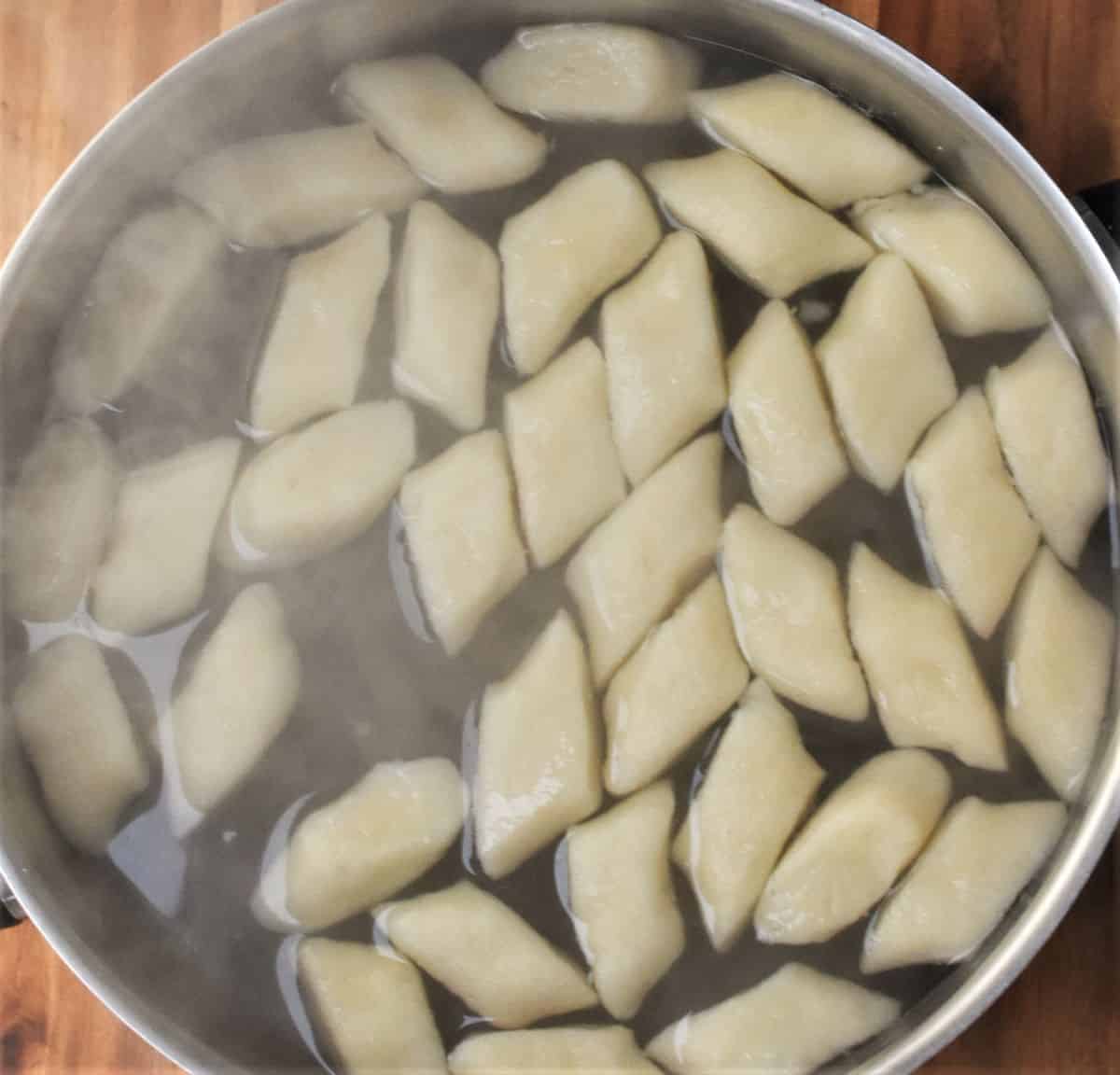 Boiling potato dumplings in large pot with steam visible.