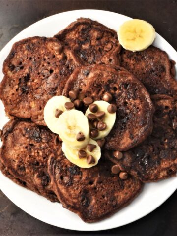 Top down view of chocolate banana pancakes on white plate with banana slices.