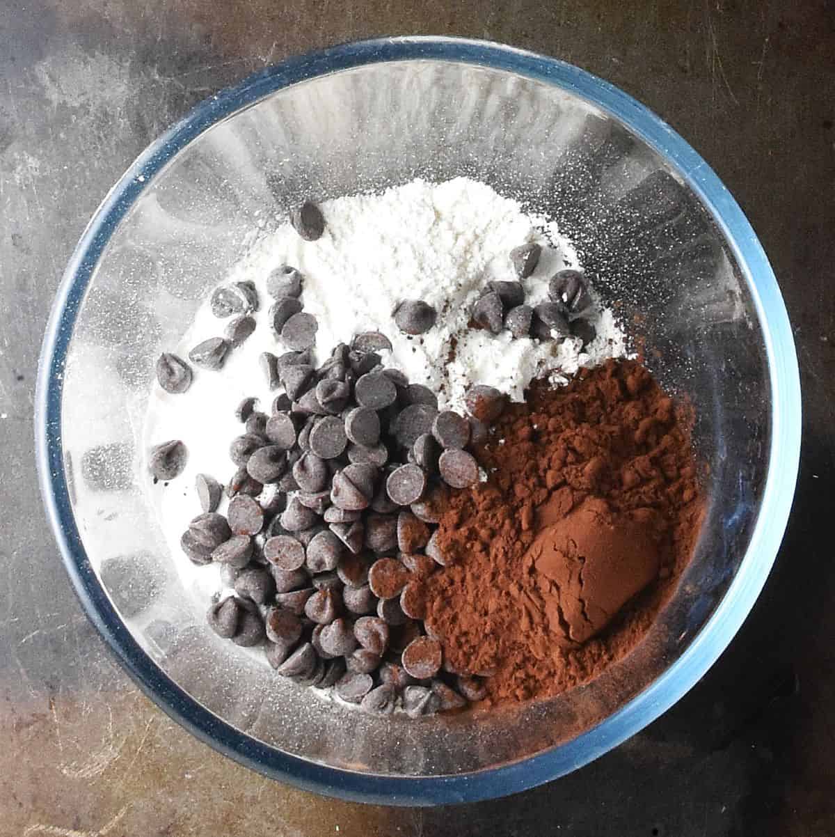 Flour, cocoa powder and chocolate chips in glass bowl.