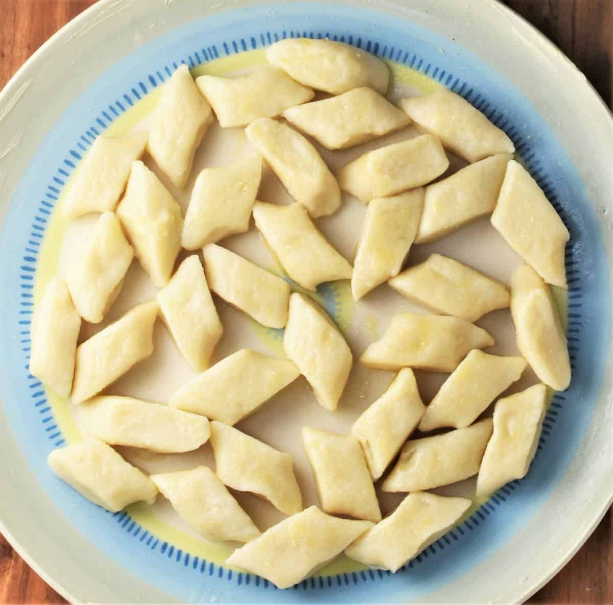 Boiled Polish potato dumplings on top of large blue plate.