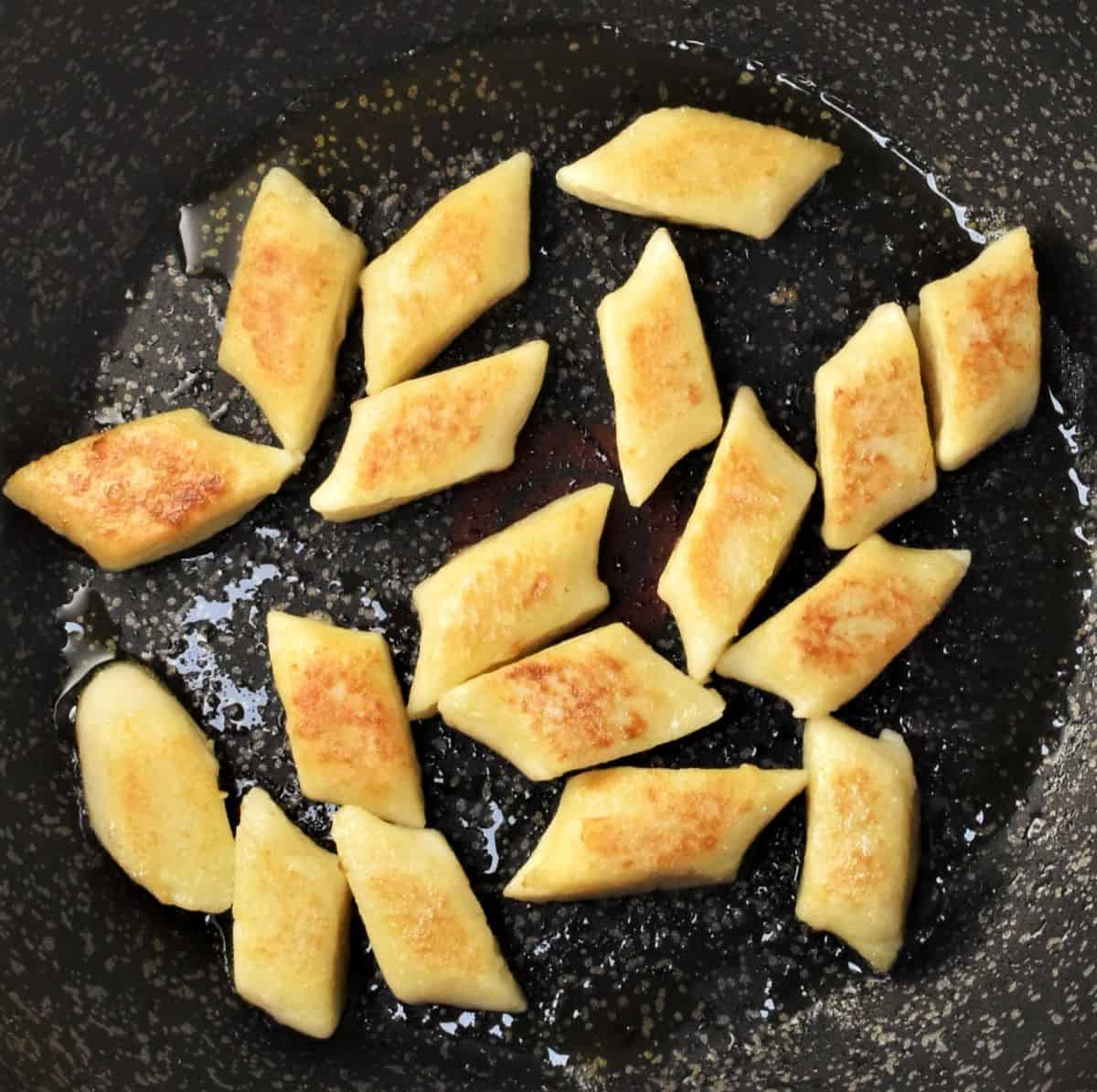 Lightly browned fried dumplings in pan.