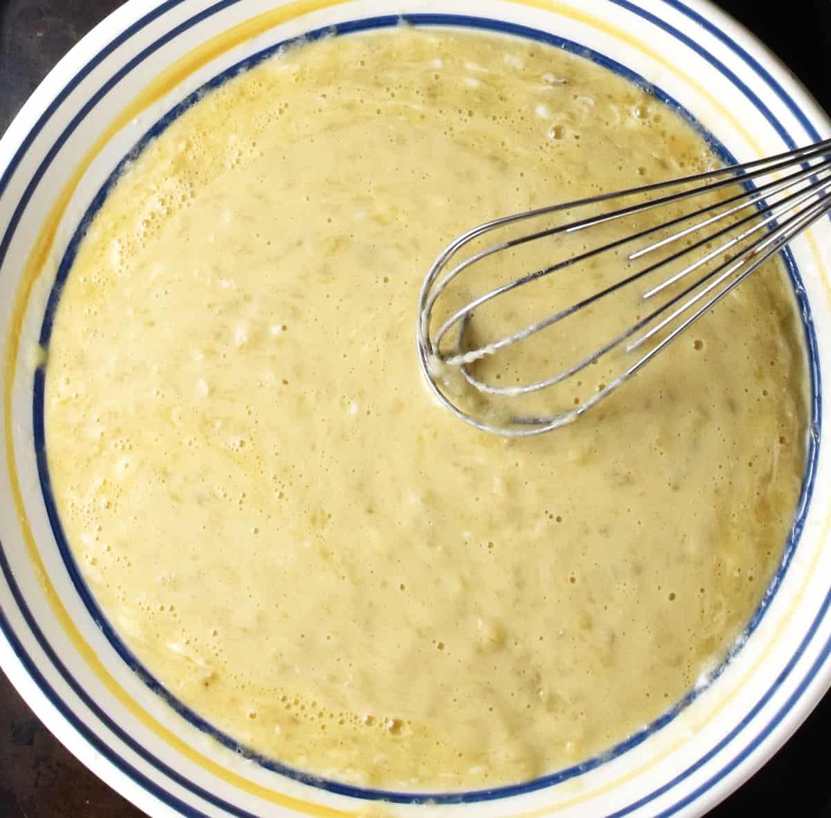 Top down view of mashed banana mixture with potato masher in large shallow bowl.