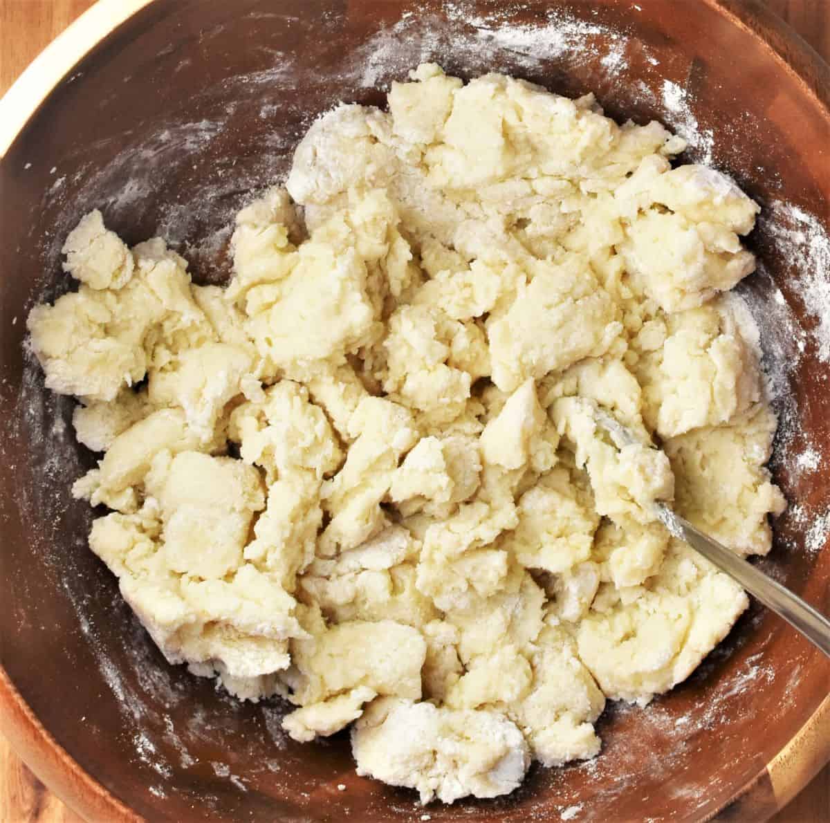 Making dough for potato dumplings in large wooden bowl.