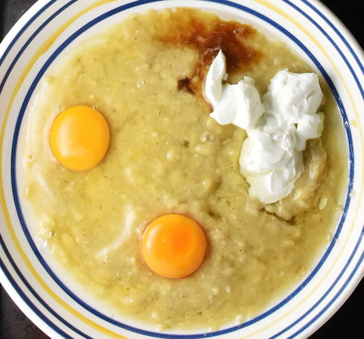 Mashed banana with 2 raw eggs and yogurt in shallow bowl.