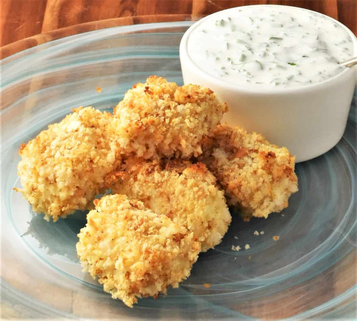 Crispy baked fish nuggets on top of plate with yogurt dip.