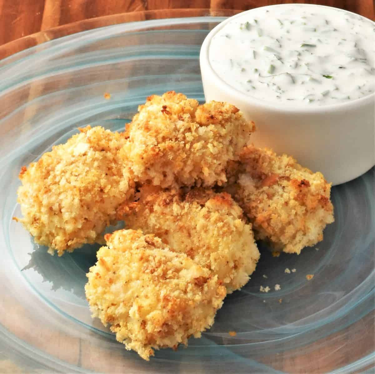 Side view of breaded fish nuggets on top of blue plate with yogurt sauce.