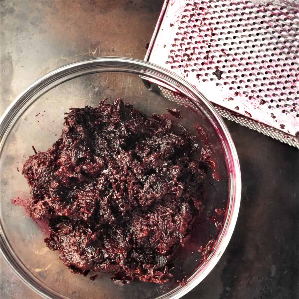 Finely grated roasted beets in bowl with box grater in background.