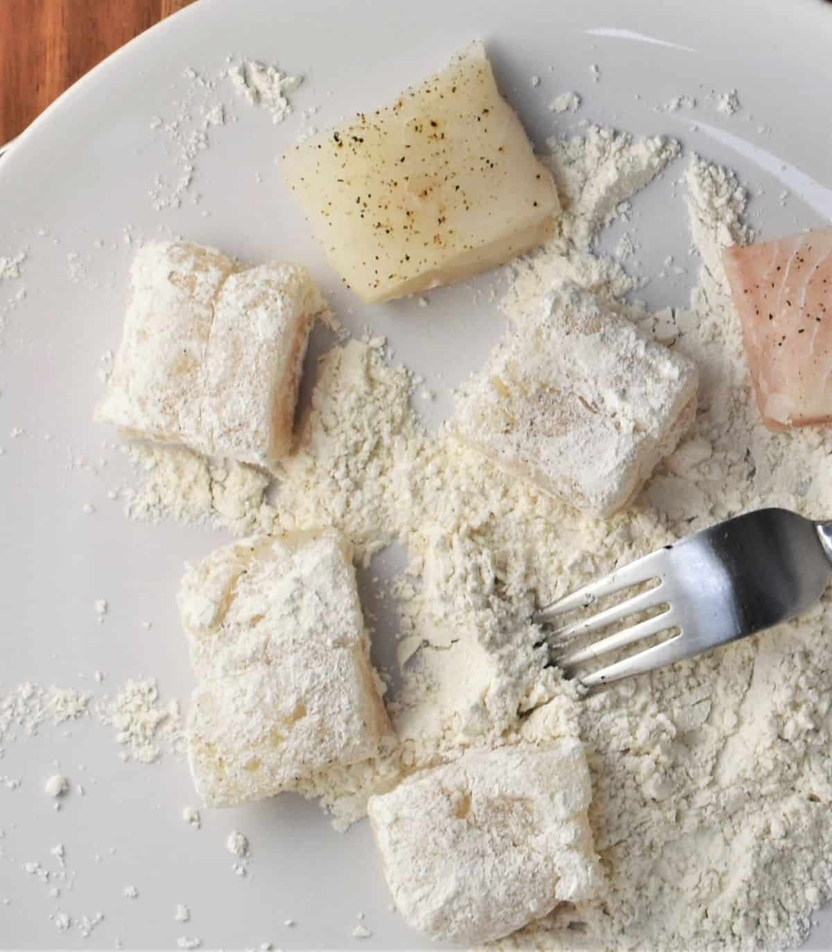 Coating fish bites in flour on top of plate.