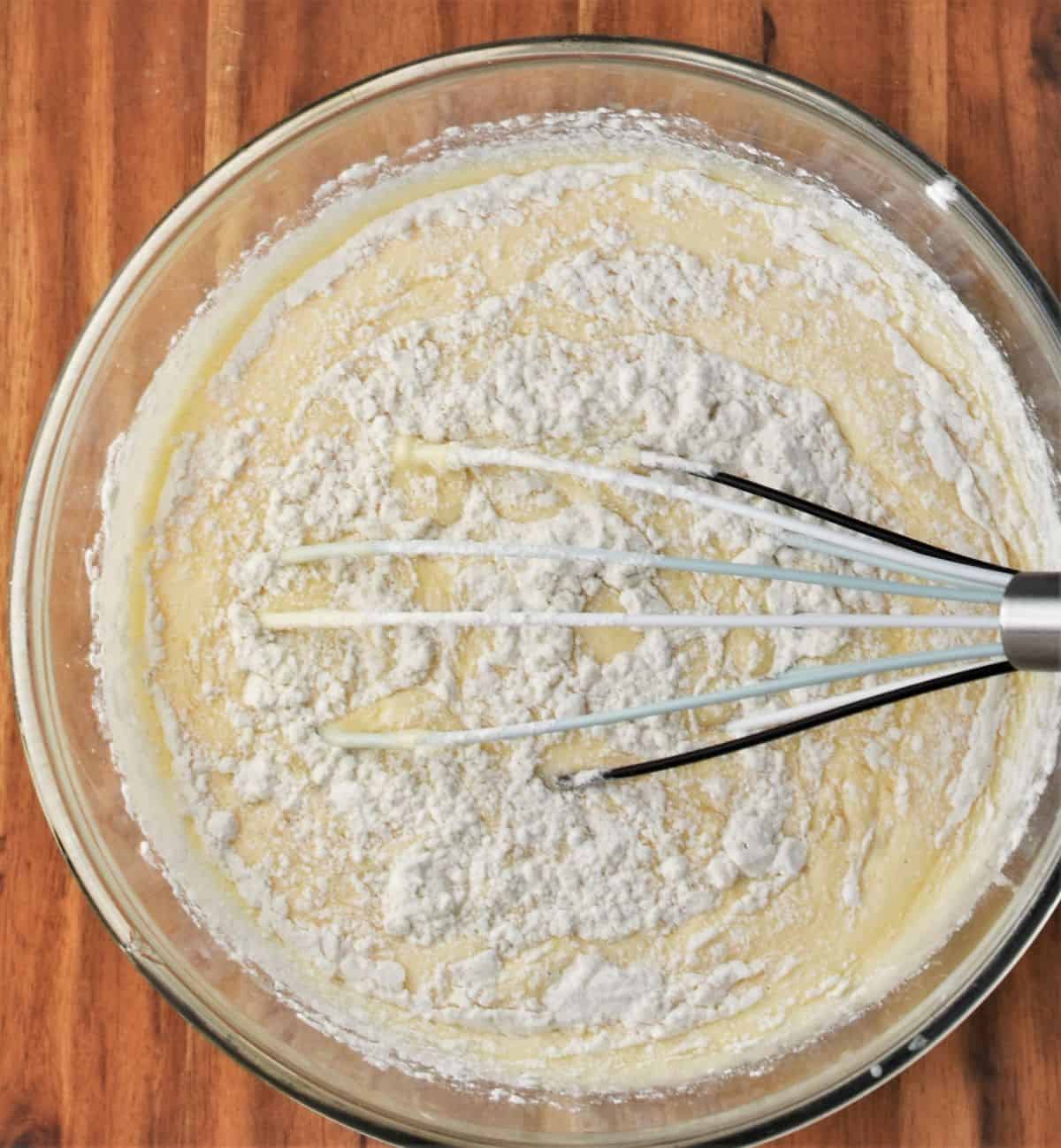 Whisking flour into batter in mixing bowl.