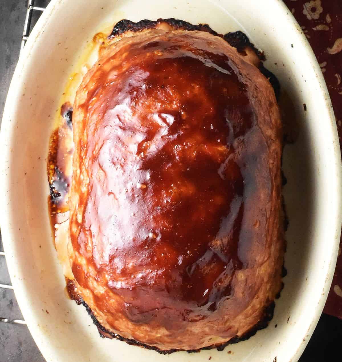 Baked meatloaf with oats with ketchup glaze in white ceramic dish.