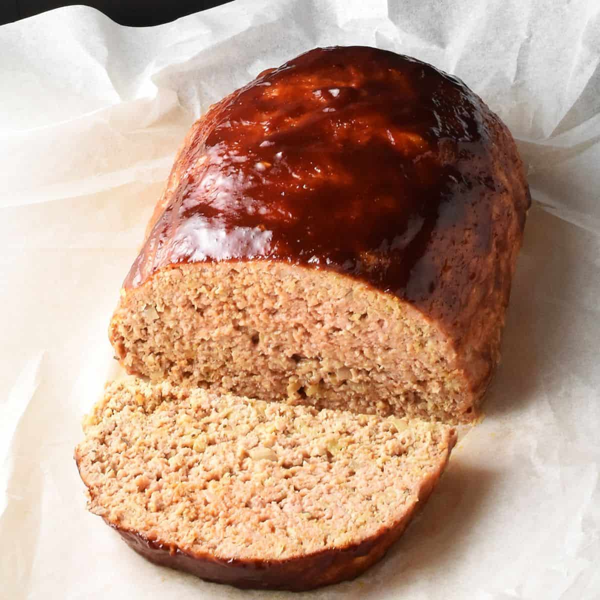 Side view of cut meatloaf with oats and glaze on parchment paper.