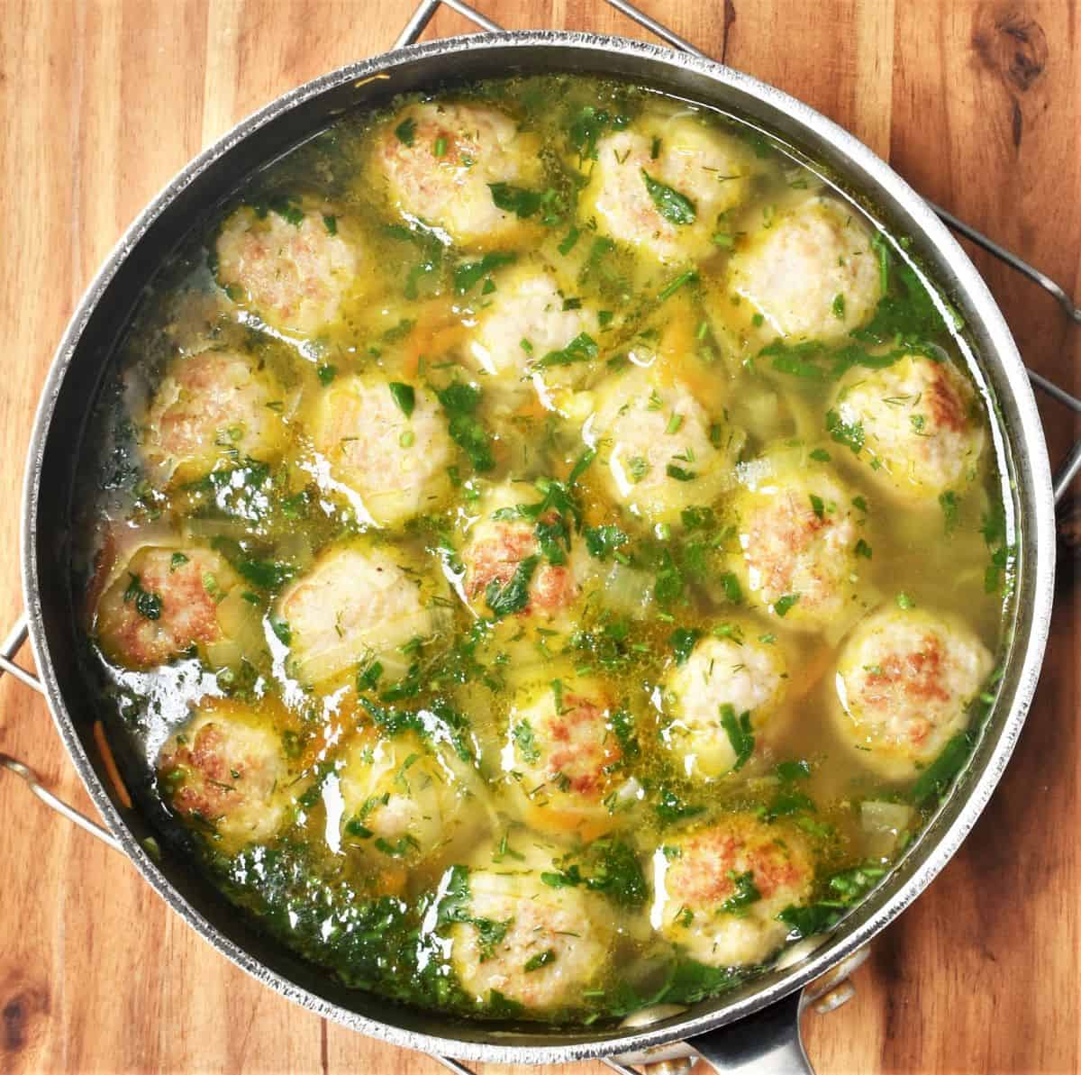 Soup with meatballs and herbs in large pot.