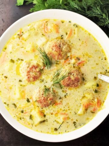 Top down view of chicken meatball soup in white bowl with spoon.