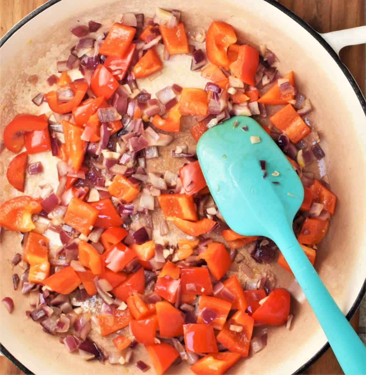 Chopped vegetables in large pan with blue spoon.