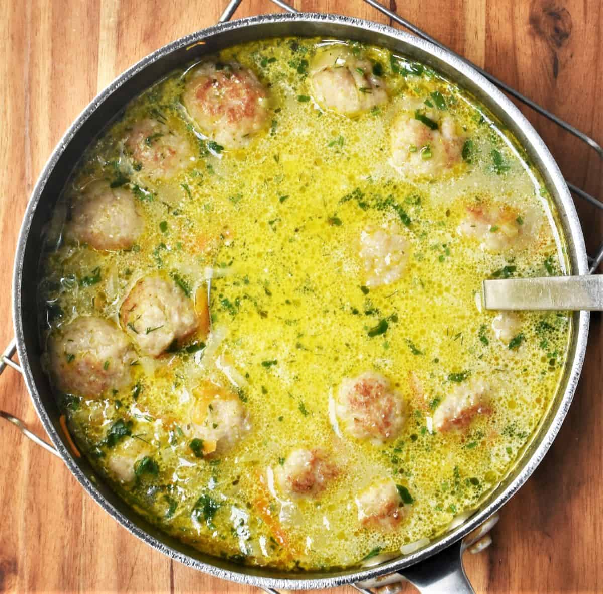 Polish chicken meatball soup with potatoes in pot with spoon.