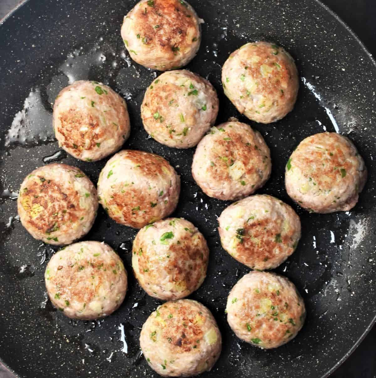 Top down view of browned meatballs in large pan.