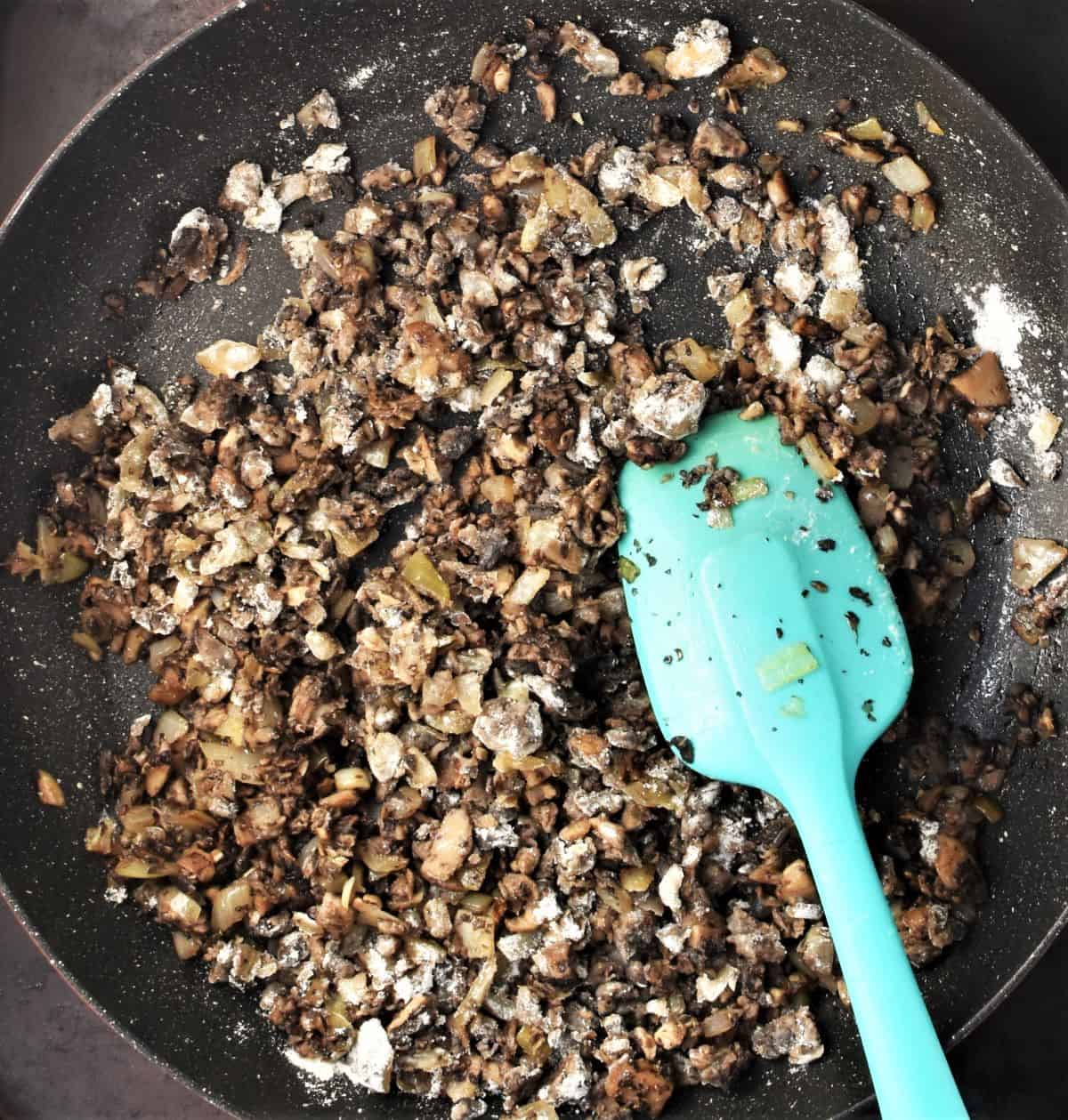 Frying chopped mushrooms in large pan with blue spoon.