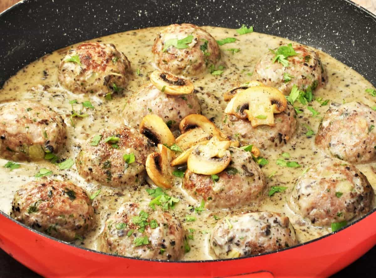 Side view of meatballs and mushroom sauce in large shallow red pan.