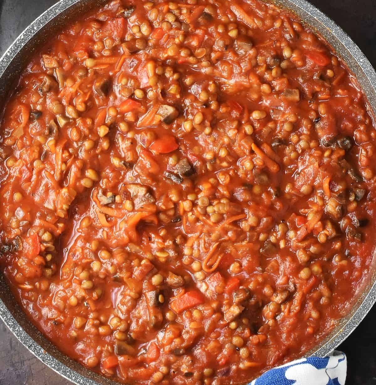 Top down view of tomato sauce with lentils in large, shallow pan.