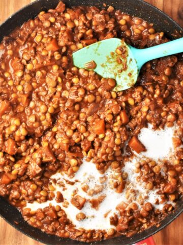 Thick lentil ragu sauce with cream in large shallow pan with blue spoon.