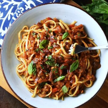 Top down view of lentil ragu with pasta in blue bowl with fork.