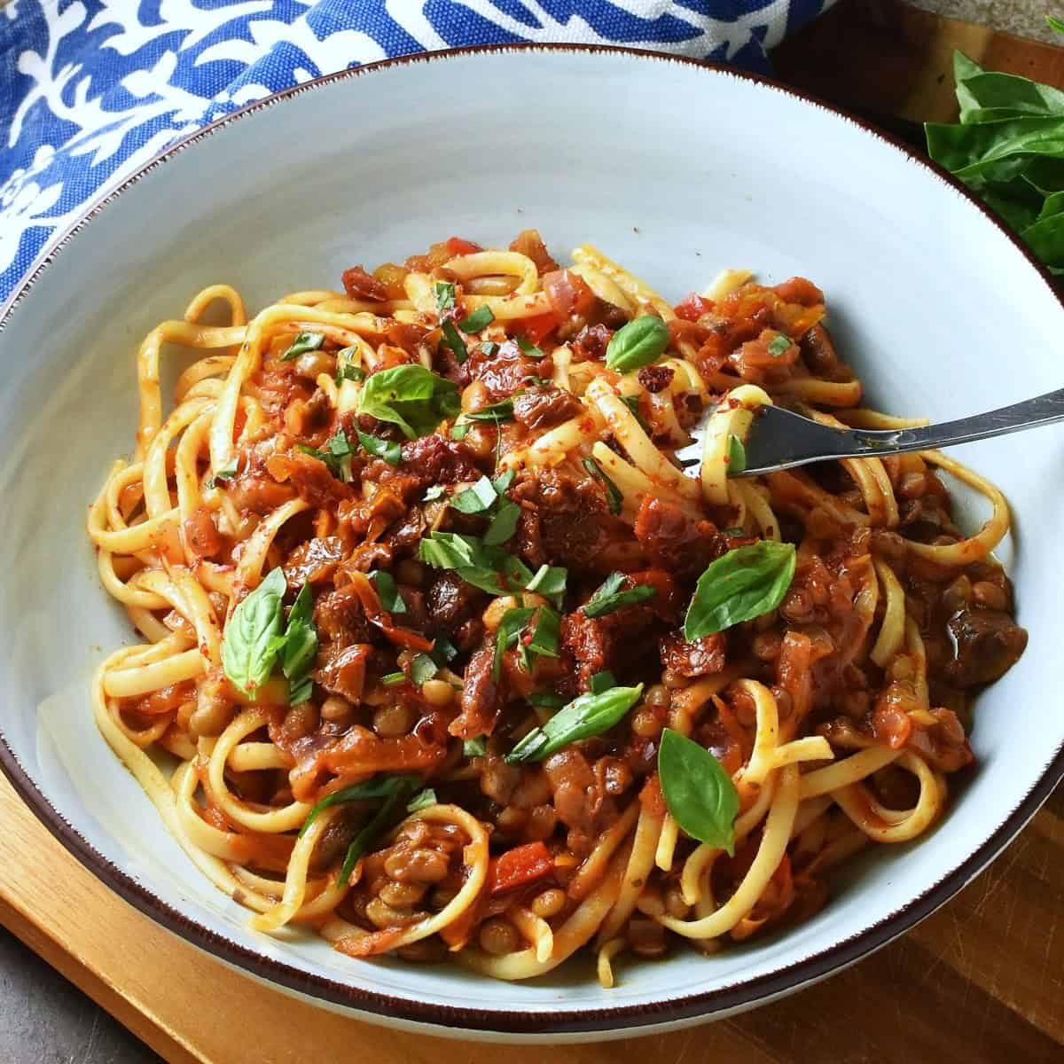 Side view of lentil tomato sauce with linguine pasta and basil in blue bowl with fork.