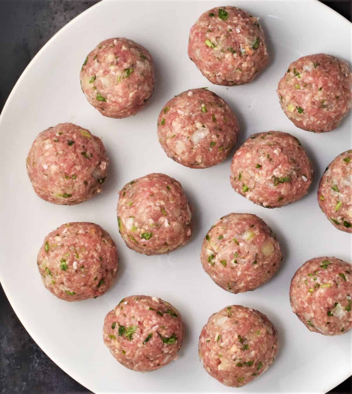 Raw meatballs on top of large white plate.