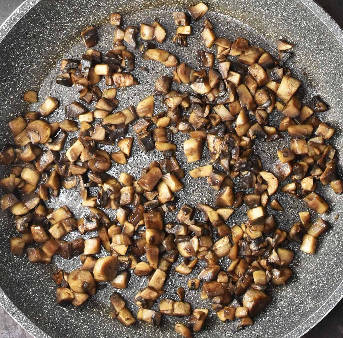 Chopped browned mushrooms in large, grey shallow pan.