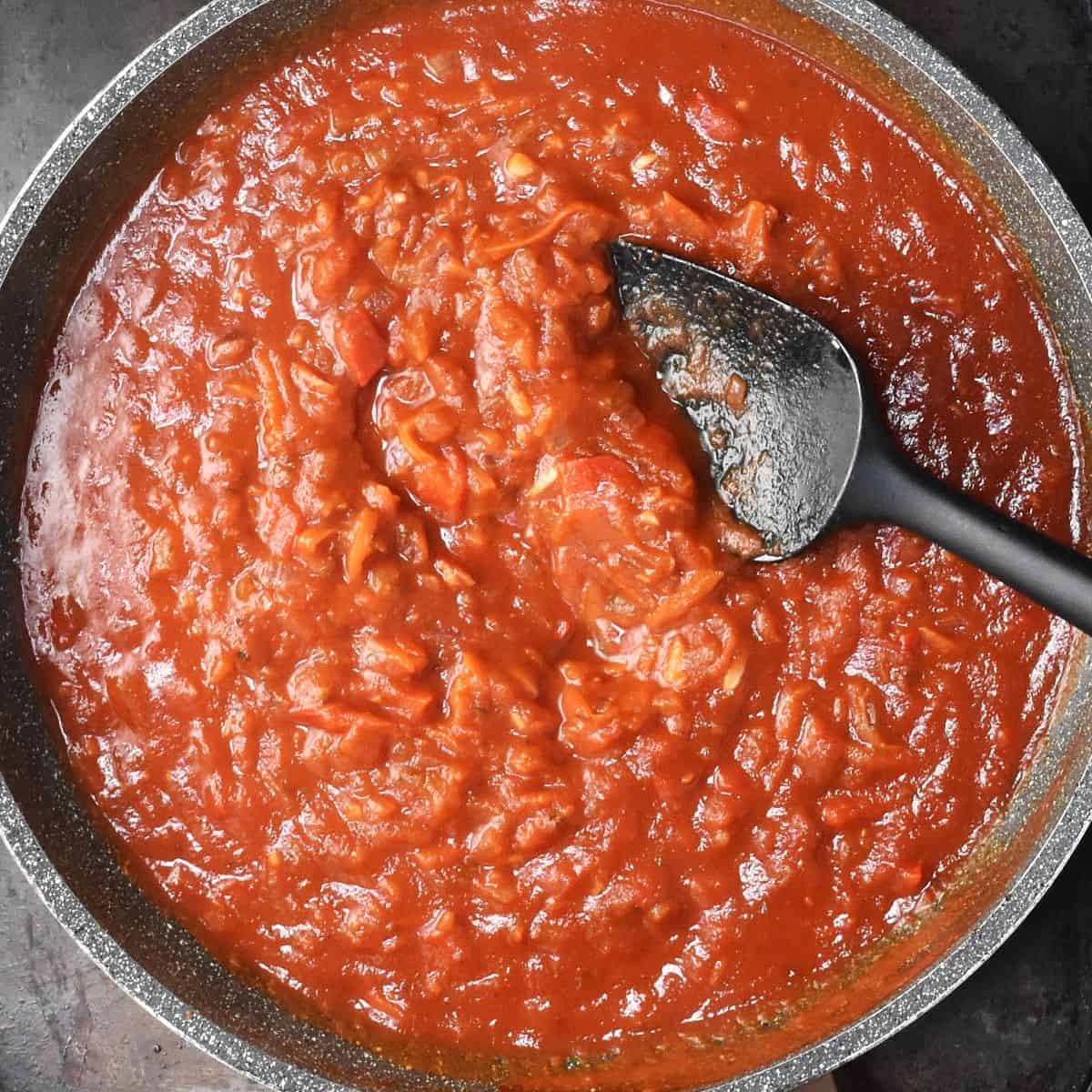Thick tomato sauce in large, gray pan with black spoon.