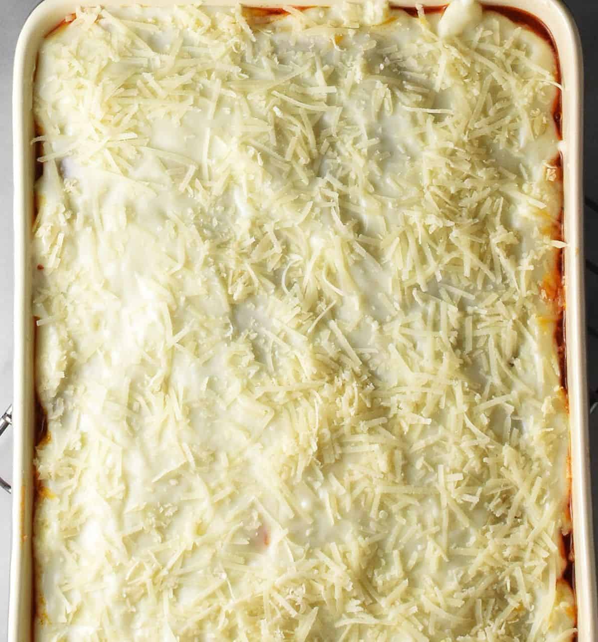 Uncooked turkey lasagna topped with white sauce and cheese.