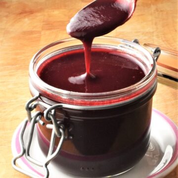 Side view of creamy blackberry sauce in jar with spoon over it.