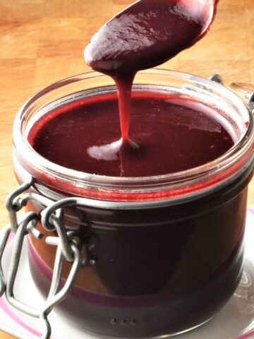 Side view of creamy blackberry sauce in jar with spoon over it.