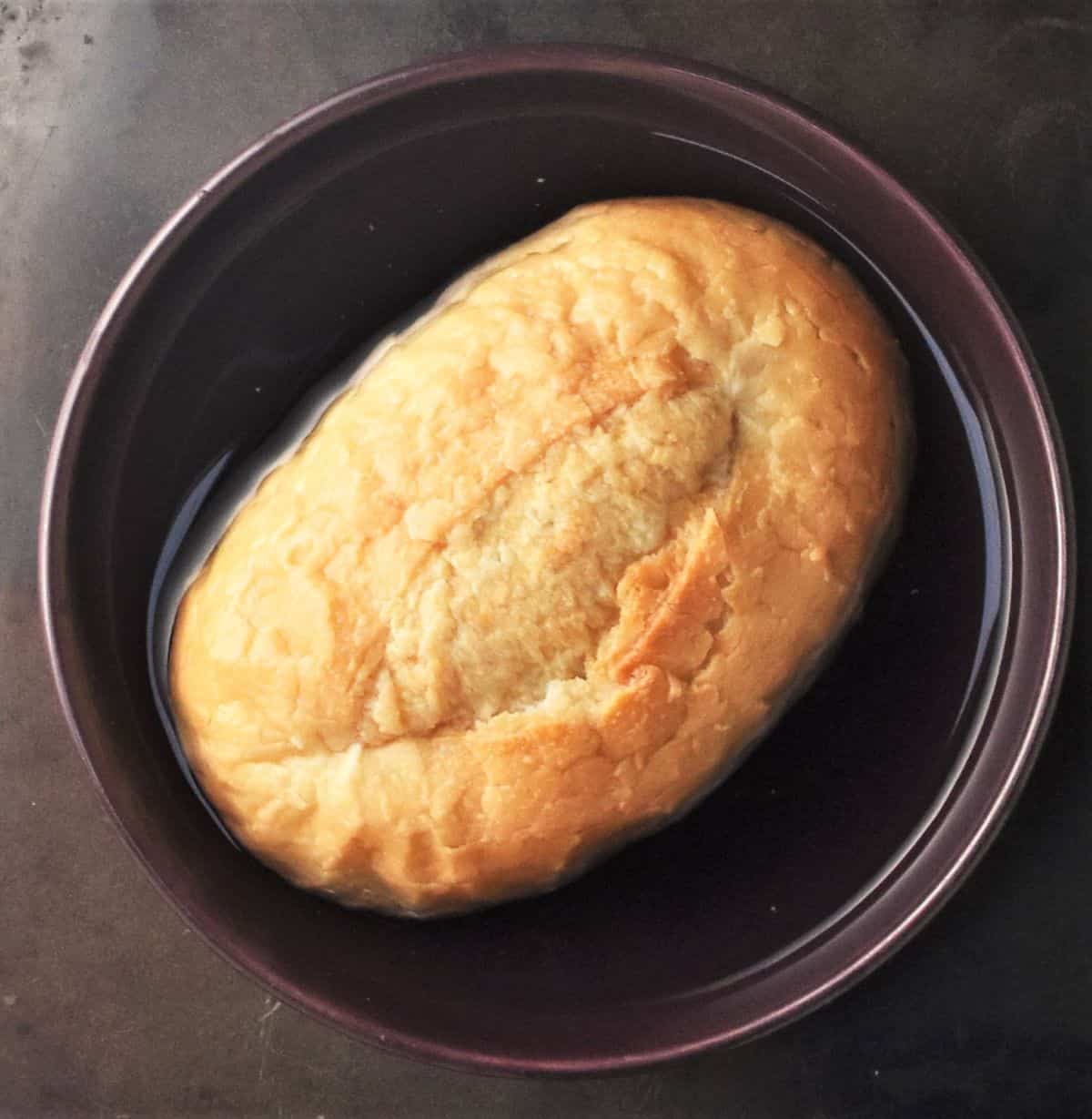 Oval bun soaking in water in bowl.