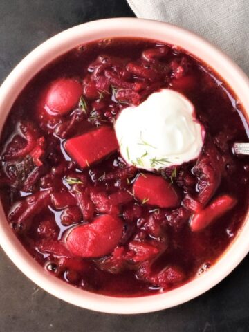 Top down view of vegetarian borscht with sour cream and spoon in pink bowl.