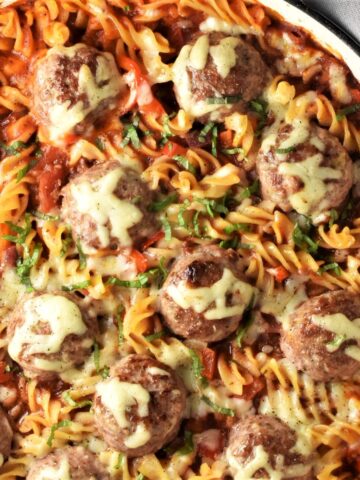 Top down view of meatball pasta bake with melted cheese in large shallow dish.