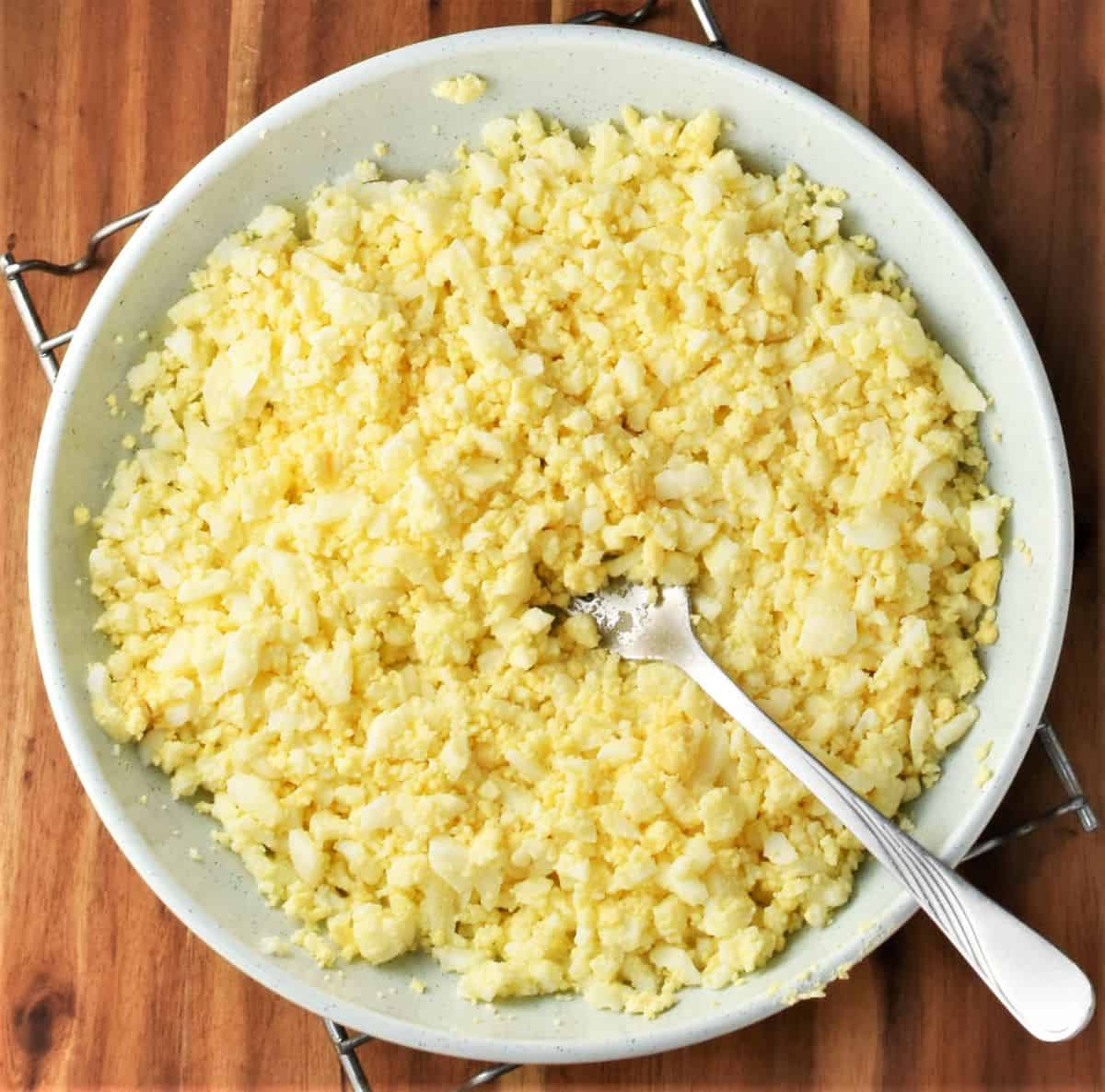 Crumbly egg mixture with fork in blue bowl.