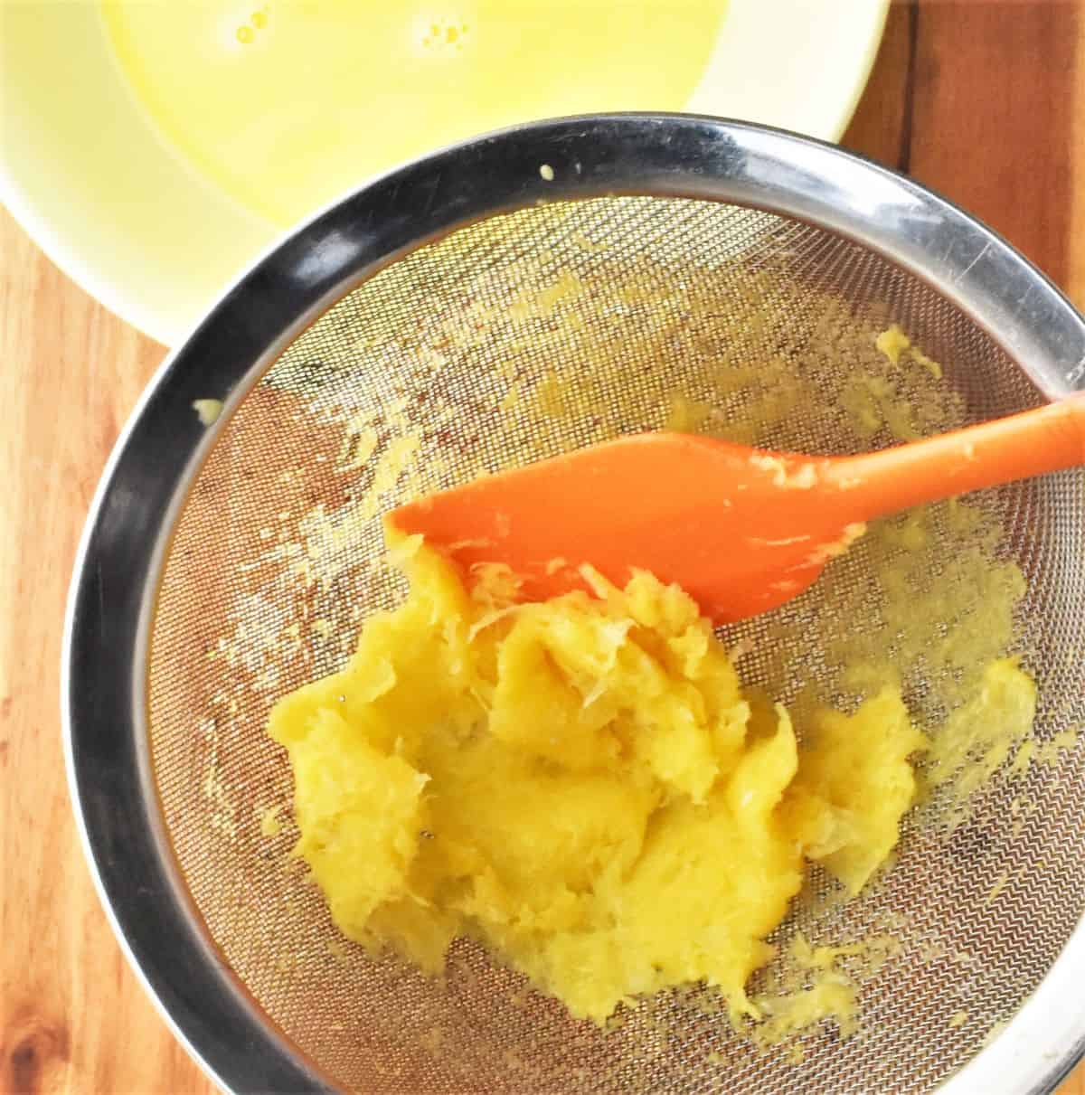 Orange pulp with orange spatula in sieve.