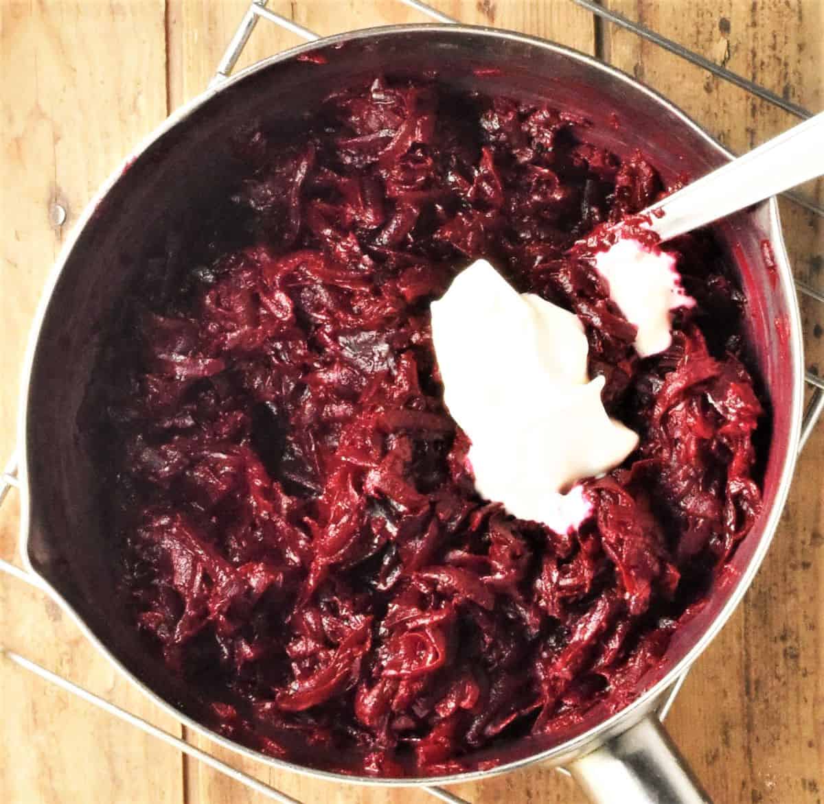 Shredded beetroot with dollop of sour cream and spoon in pan.