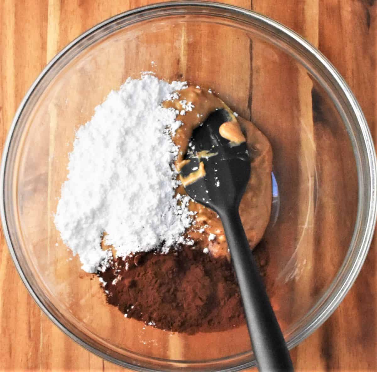 Peanut butter, cocoa and sugar in bowl with spatula.
