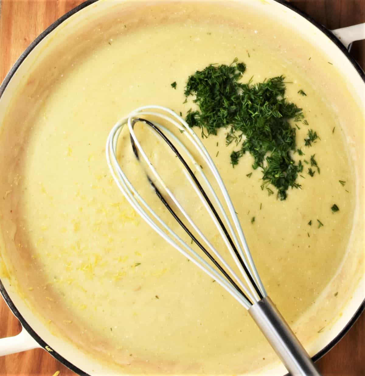Creamy white sauce with dill and whisk in shallow pan.