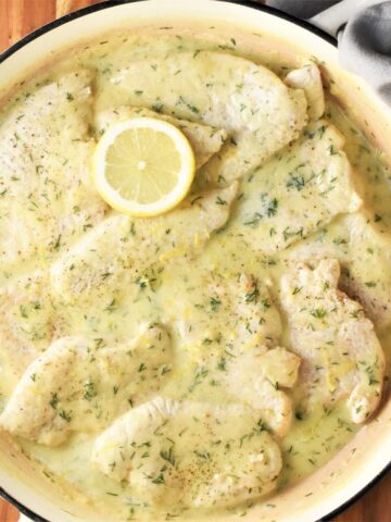 Top down view of turkey steaks in creamy sauce in large shallow pan.