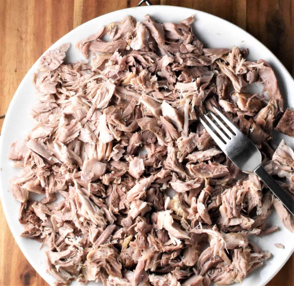 Chopped cooked meat on large plate with fork.