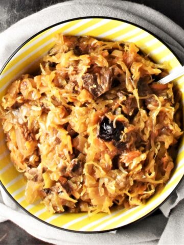 Top down view of sauerkraut with mushrooms in yellow bowl with spoon.