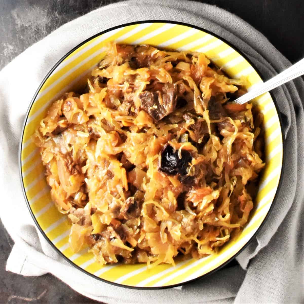 Top down view of sauerkraut with mushrooms in yellow bowl with spoon.